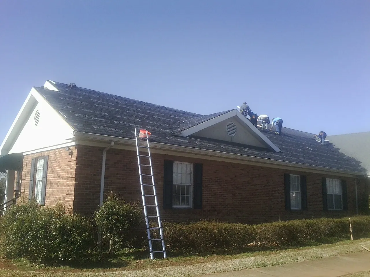 Crew tearing shingles off a brick ranch roof with a ladder set — Metal Roof Repair work by our crew in Tarzana