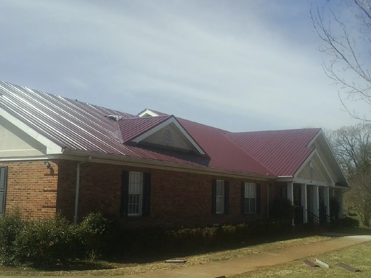 Red metal roof with gabled entries on a long brick building, from a Hail Damage Roof Repair job in Tarzana