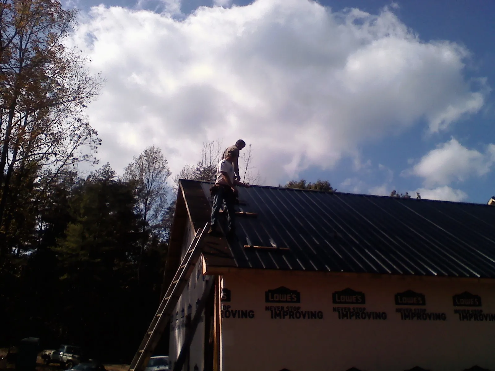 Roofer fastening dark metal panels high against a cloudy sky, from a Roof Inspection job in Tarzana